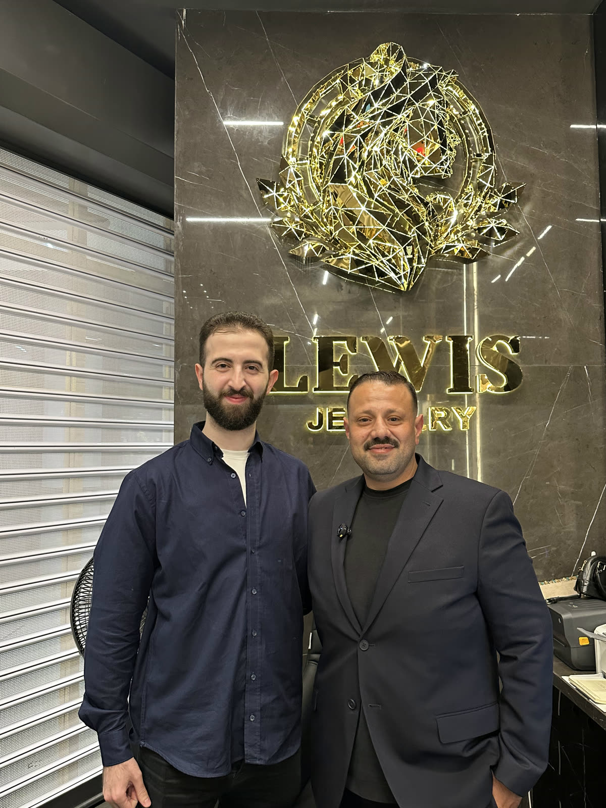 زميلان أمام جدار العلامة التجارية لـ Lewis Jewelry داخل الفرع الجديد.