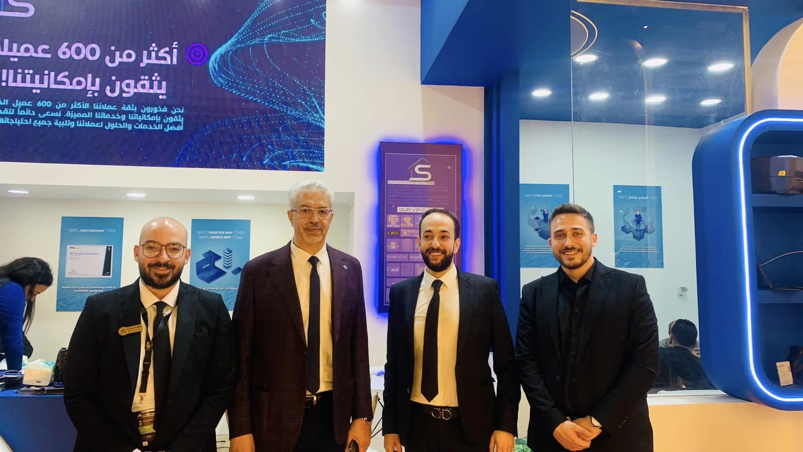 أربعة من أعضاء فريق SWH أمام جدار العرض في الجناح بمعرض NEBU 2023.